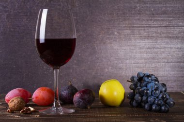 Bardak kırmızı şarap, peynir, üzüm, ceviz, incir, Erik ve elma ahşap arka plan üzerinde