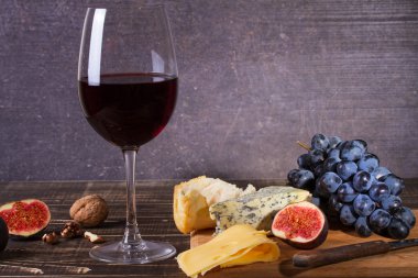 Bardak kırmızı şarap, peynir, üzüm, ceviz, incir, Erik ve elma ahşap arka plan üzerinde