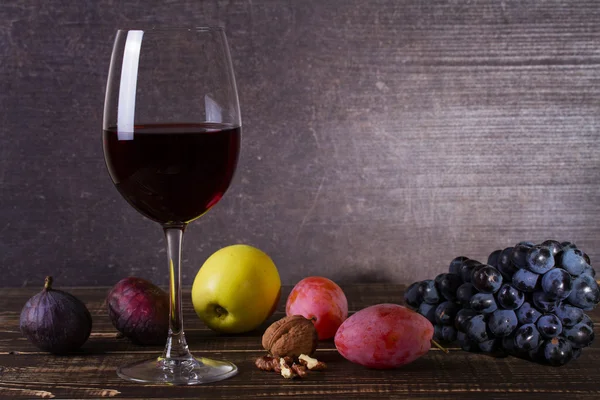 Bicchiere di vino rosso, formaggio, uva, noci, fichi, prugne e mela su fondo di legno — Foto Stock