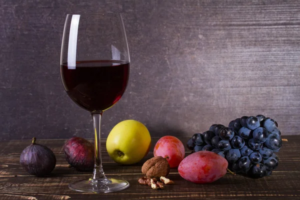 Bicchiere di vino rosso, formaggio, uva, noci, fichi, prugne e mela su fondo di legno — Foto Stock