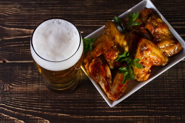 Vaso de cerveza y alitas de pollo sobre fondo de madera oscura —  Fotos de Stock