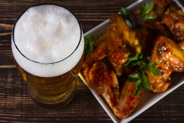 Vaso de cerveza y alitas de pollo sobre fondo de madera oscura — Foto de Stock