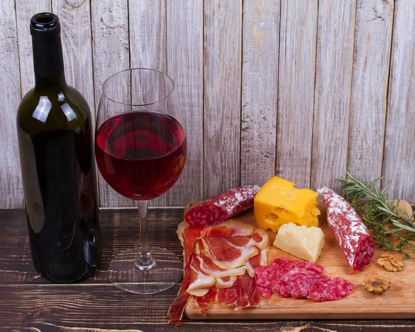 Verre et bouteille de vin rouge, fromage, salami, noix, prosciutto et romarin sur fond de bois — Photo