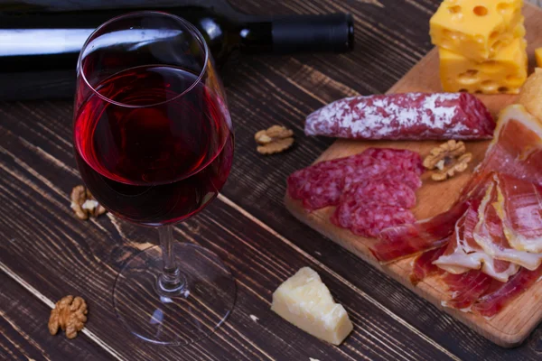 Verre et bouteille de vin rouge, fromage, salami, noix, prosciutto et romarin sur fond de bois — Photo