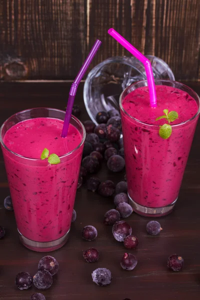 Frozen summer berries smoothie garnished with mint on dark wooden background