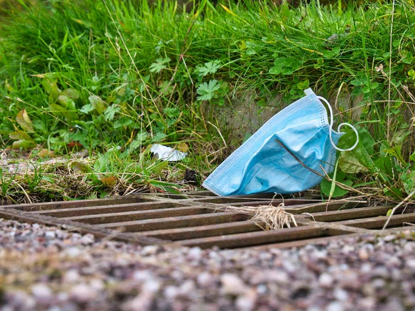A used, blue surgical face mask used for COVID-19 PPE protection, discarded as litter on a pavement / sidewalk in an urban area causing environmental pollution