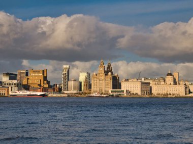 Liverpool 'un UNESCO limanına demirlemiş olan Man Adası ve Mersey Feribotları kıyıda listelenmiştir. Kraliyet Karaciğeri, Cunard & Liverpool Binaları sağda - Üç Zarafet.