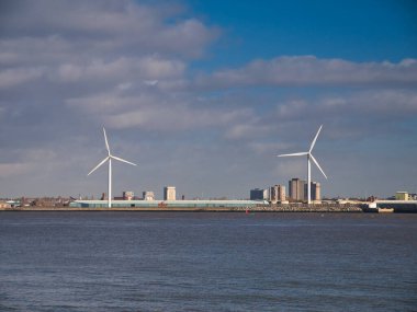 İngiltere 'nin kuzeybatısındaki Liverpool' da Mersey Nehri 'nin kuzey kıyısında iki karadan rüzgar türbini. Sonbaharda güneşli bir günde çekilmiş..