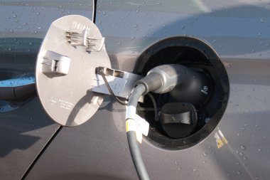 Bir süpermarket otoparkında bir hibrit araba bir EV (elektrikli araç) şarj cihazı kullanır. Elektrik şarj konnektörü (bağlı) ve benzin veya dizel dolgusu her ikisi de görünür.