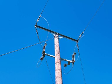 Birleşik Krallık ulusal şebekesinden elektrik sağlayan bir elektrik direği güç kablolarını, izolatörleri ve diğer ekipmanları gösteriyor. Güneşli bir günde, mavi bir gökyüzünde çekildi..