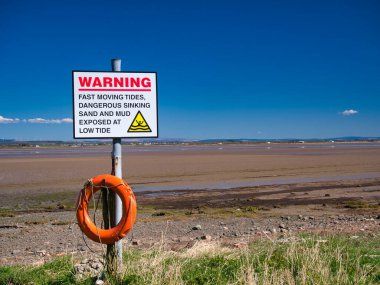Cumbria Solway Sahili 'nin kuzeybatısında alçak gelgitlerde kum ve çamurun battığı yönünde bir işaret var. Güneşli bir günde çekilmiş haliçlerin kumlarını gösterirken.