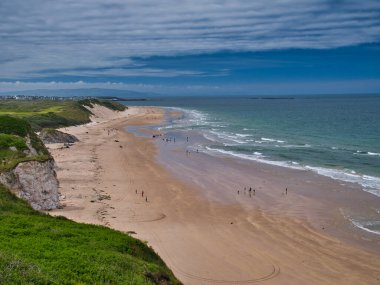 Kuzey İrlanda 'daki Whiterocks Sahili' nin el değmemiş kumu ve Antrim Geçidi kıyısındaki sahil kayalıkları. Yazın güneşli bir günde, açık bulutlar ve mavi gökyüzüyle çekildi..