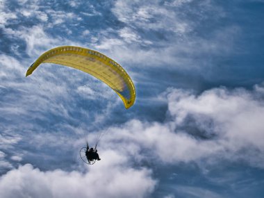 Bir pilot, Kuzey İrlanda 'nın Atlantik kıyısında Benone Strand (Sahili) üzerinde sarı bir paraşütçü uçuruyor. Güneşli bir günde çekilmiş beyaz bulutlarla.