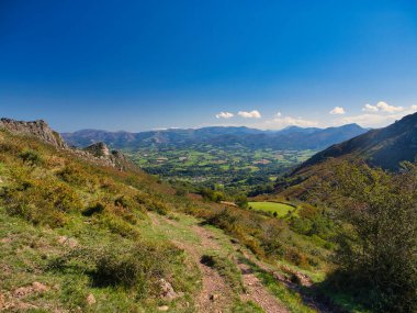 Fransa 'nın Bask Bölgesi' nde Sare yakınlarında, koyu mavi gökyüzünün altındaki Pireneler ve yeşil vadilerin sonbahar manzarası. Önplanda yürüyüş yolu.