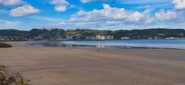 Hendaye, Fransa 'nın geniş dalgalı kumları, parlak gökyüzünün ve dalgalı bulutların altında Spains kıyıları. Yürüyüşçüler ölçek ekler ve sakin bir hava katar..
