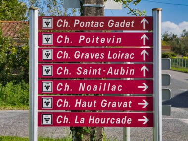 Medoc, Fransa - 05 Ekim 2025: Kırmızı yol kenarı işaretleri, Fransa 'nın Medoc kentindeki şarap rotası boyunca, parlak bir öğleden sonra gökyüzünün altında bulunan birkaç şatoyu işaret ediyor..