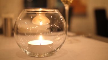 Masanın üzerinde duran küçük bir mum romantik bir atmosfer yaratıyor. Işıklar ve ateş cama yansıyor. Mum alevi kadehin içinde yavaşça sallanıyor ve Noel huzuru yaratıyor.