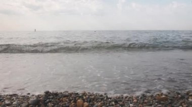 Okyanusun köpüklü dalgalarıyla yıkanmış küçük çakıl taşlarından oluşan taştan bir kumsal. Sakin bir denizin üzerinde berrak bir yaz günü