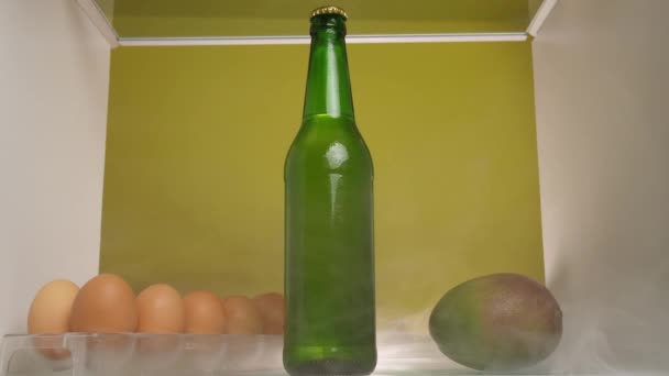 白い男が冷蔵庫に入ってきて冷蔵庫に入った緑色の瓶を探します 冷蔵庫には煙が充満していて棚の上の新鮮な果物の上にゆっくりと広がり — ストック動画