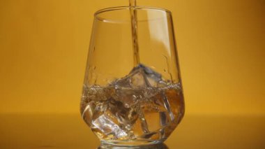 Alkolik bir içecek, içinde buz küpleri olan bir bardağa dökülür. Alkolik bir içecek, içinde buz küpleri olan bir bardağa dökülür. Yavaş çekim yakın çekim