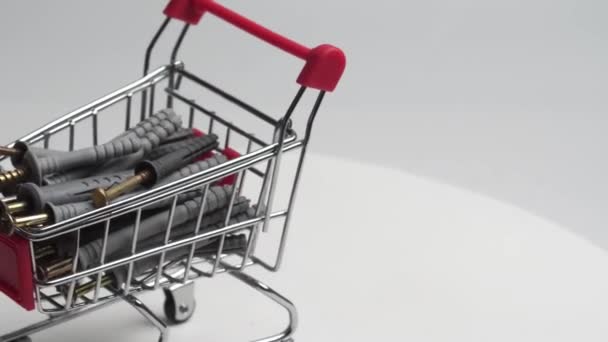白い背景でボルトとネジで満たされたスーパーからのミニチュアショッピングカートがゆっくりと回転します 詳細な計画を — ストック動画