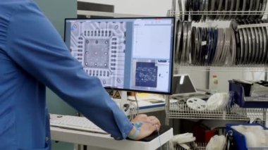 Fabrikada çalışan bir işçi bilgisayar monitörünün önünde duruyor ve elektrik devrelerine bakıyor. Modern bir kuruluşta işlemci ve anakart üretimi
