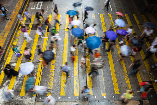 Motion blurred pedestrians crossing Hong Kong street in the rain