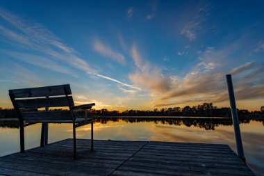Beautiful sunset reflecting on the water at the public boat landing and dock with bench on Little Moon Lake, Barron County WI clipart