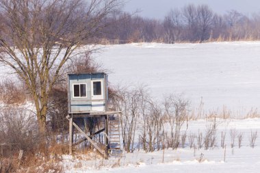 Homemade elevated hunting blind during winter with snow. Selective focus, background blur and foreground blur.