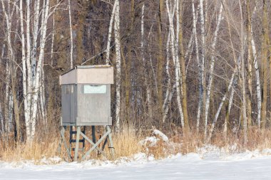Homemade elevated hunting blind during winter with snow. Selective focus, background blur and foreground blur.