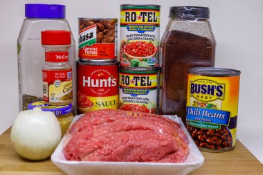 Dunn County, WI, ABD - 1 Ocak 2021: Beyaz arka planda izole edilmiş, ahşap bir kesme tahtasına kırmızı biber yapmak için gerekli malzemeler. İçindekiler arasında hamburger, soğan, kekik, biber tozu, kimyon, sarımsak, doğranmış domates, domates sosu yer alıyor., 