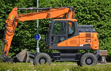 Yeşil çalıların önündeki yolda kazıcı var.