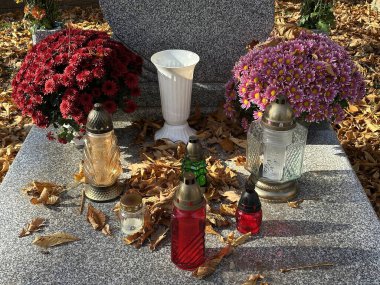 Halk mezarlığındaki bir mezar taşında çiçekler ve mumlar.