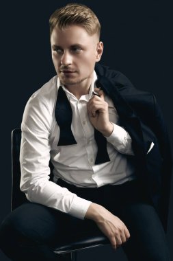 Siyah stüdyo arka planında poz veren zarif smokinli ve papyonlu yakışıklı sarışın adam portresi.