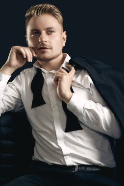 Siyah stüdyo arka planında poz veren zarif smokinli ve papyonlu yakışıklı sarışın adam portresi.