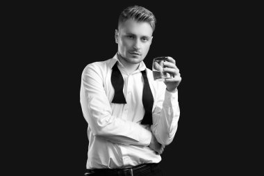 Zarif smokinli ve papyonlu yakışıklı sarışının portresi. Siyah stüdyo arka planında viski bardağıyla poz veriyor.