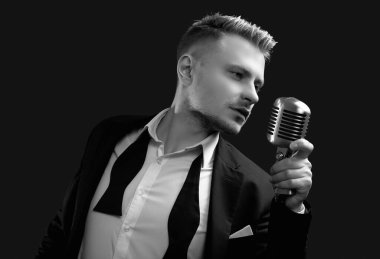 Siyah stüdyo arka planında klasik mikrofonla poz veren zarif smokinli ve papyonlu yakışıklı sarışın adam portresi