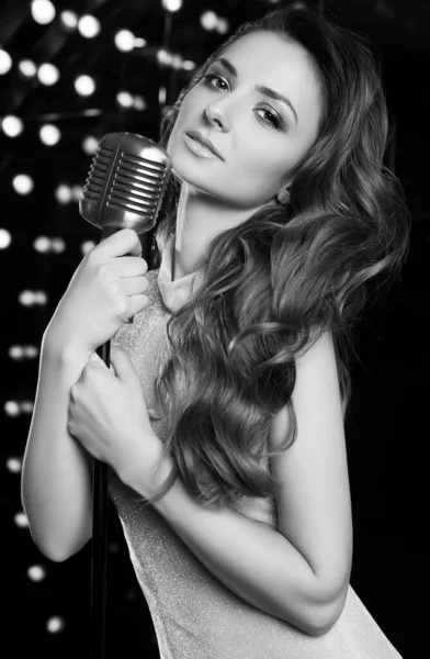 Portrait of gorgeous singer woman in elegant dress with retro microphone on restaurant stage spotlights background.