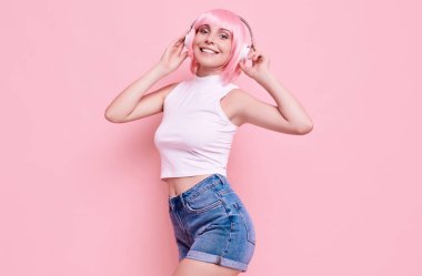 Pembe saçlı, parlak, seksi hippi kızın portresi renkli arka planda kulaklıkla müzik dinlemekten hoşlanıyor.