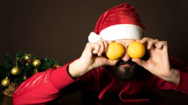 Genç, modern Noel Baba ağacın yanında bir masada oturuyor. Duygusal bir portre. Noel zamanı. Mandalina