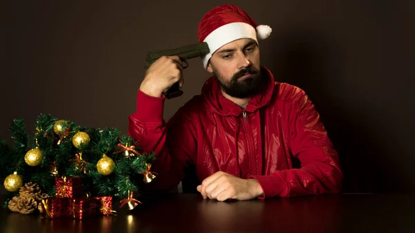 Genç, modern Noel Baba ağacın yanında bir masada oturuyor. Duygusal bir portre. Noel zamanı. Tabanca.