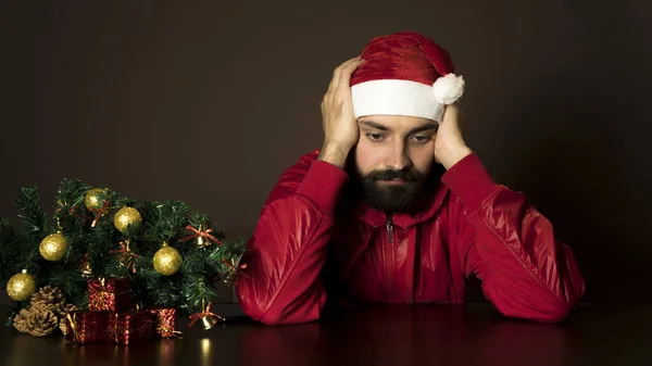 Genç, modern Noel Baba ağacın yanında bir masada oturuyor. Duygusal bir portre. Noel
