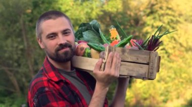 Çiftçi, sebze dolu tahta bir kutuyla organik tarlada yürüyor. Bahçedeki gülümseyen beyaz sakallı adamın portresi. Ağır çekimde yakın çekim.