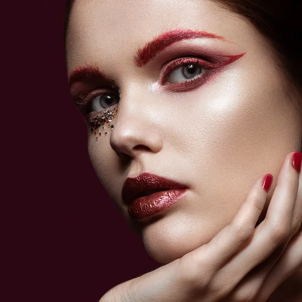 Bella ragazza con un trucco di moda rosso brillante e cristalli sul viso. Ritratto ravvicinato . — Foto Stock