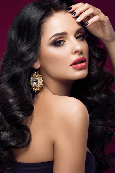Beautiful brunette model: curls, classic makeup, gold jewelry and red lips. The beauty face.