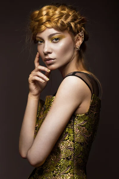 Mooi meisje in een gouden jurk met creatieve make-up en vlechten op haar hoofd. De schoonheid van het gezicht. — Stockfoto