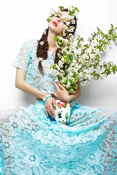 Menina morena bonita em vestido de verão azul com uma maquiagem romântica suave, lábios cor de rosa, segurando flores. A beleza do rosto . — Fotografia de Stock