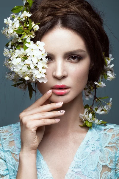 Belle fille brune en robe bleue avec un doux maquillage romantique, lèvres roses et fleurs. La beauté du visage . — Photo