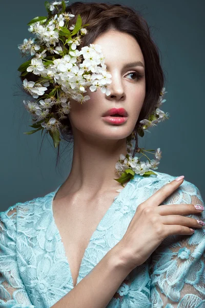 Schöne brünette Mädchen in blauem Kleid mit einem sanften romantischen Make-up, rosa Lippen und Blumen. die Schönheit des Gesichts. — Stockfoto