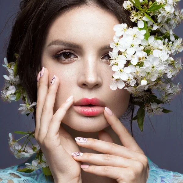 Mooie brunette meisje in blauwe jurk met een zachte romantische make-up, roze lippen en bloemen. De schoonheid van het gezicht. — Stockfoto